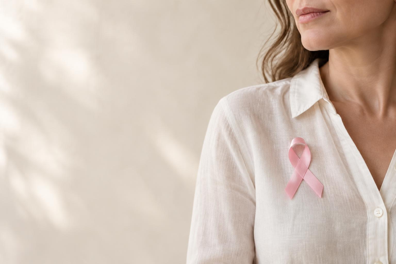 Ruban rose discret porté sur une blouse en lin ivoire, symbole de sensibilisation au cancer du sein